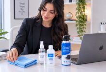 arranging a laptop screen cleaning kit with microfiber cloth, spray bottle, and alcohol on a pastel studio desk